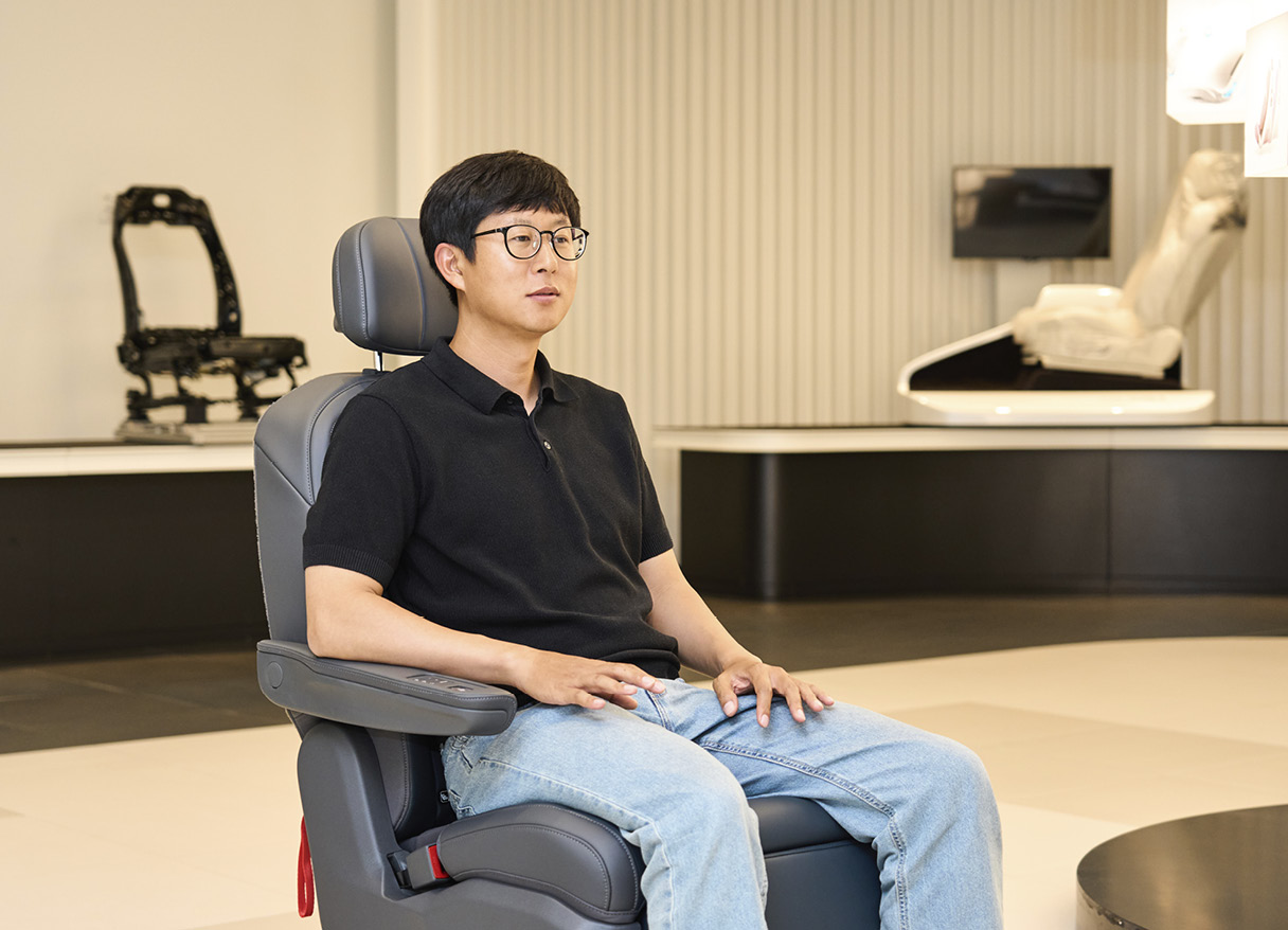 Senior researcher Hyun-seok Song is sitting on the seat and explaining its function