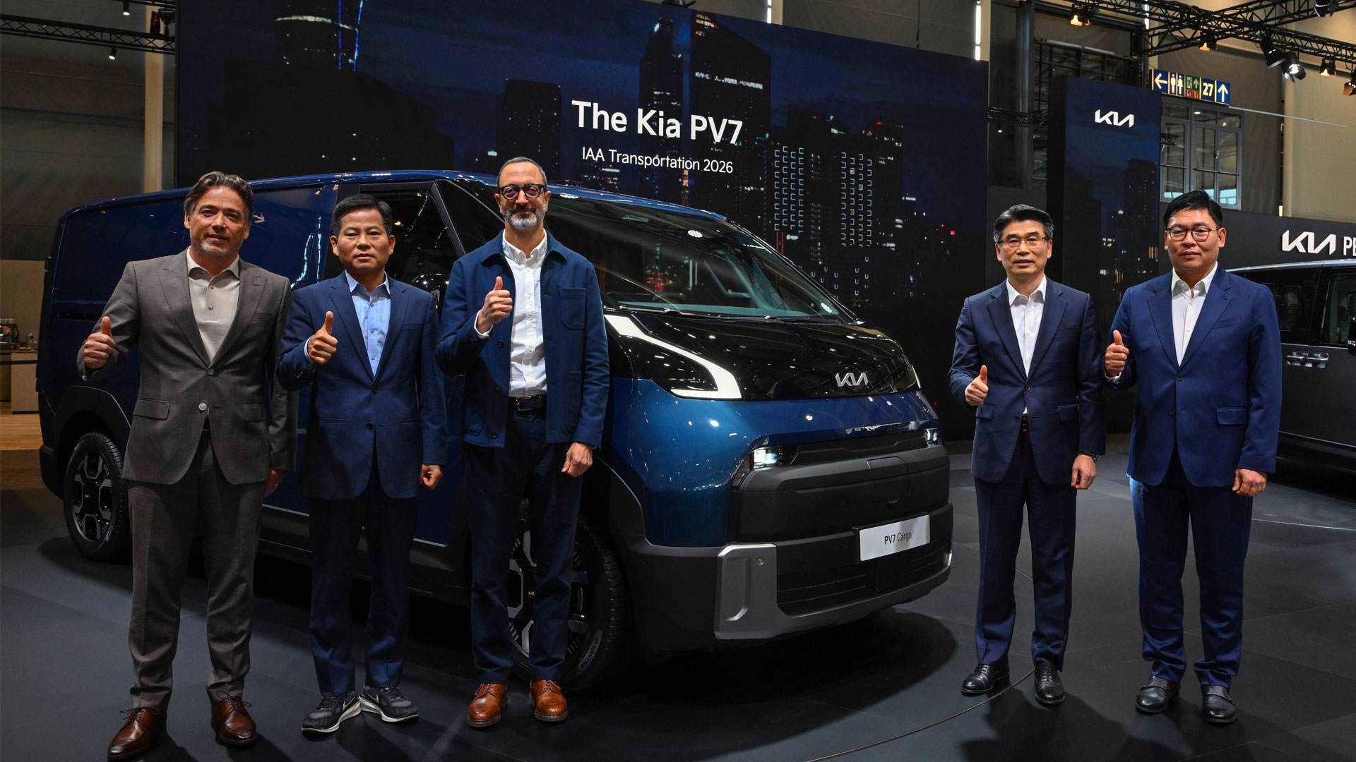 Five executives giving thumbs-up in front of a Kia PV7 Cargo van at an exhibition stage
