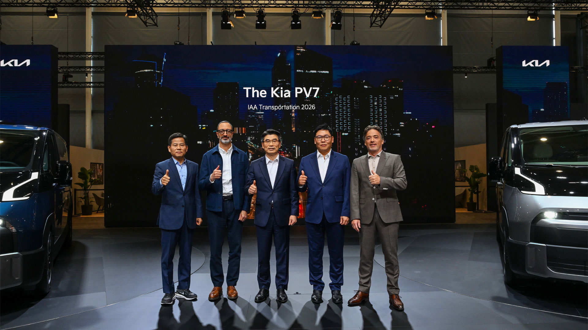 Five executives giving thumbs-up between dark blue and silver Kia vans at The Kia PV7 stage