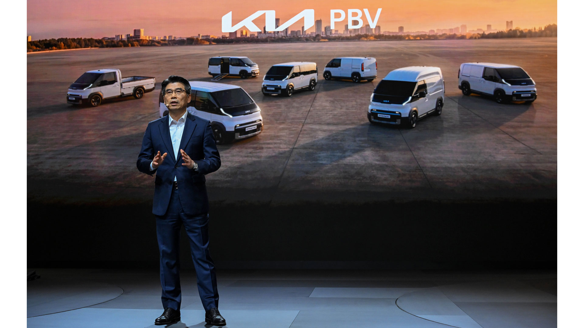 Presenter before a screen showing seven white Kia PBV concept vehicles at sunset