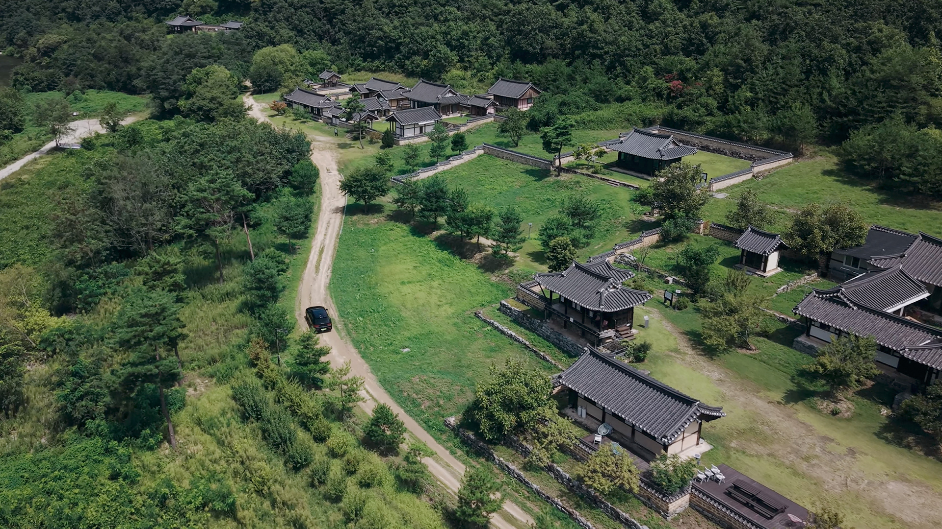 A lush wooded path and view of a traditional hanok