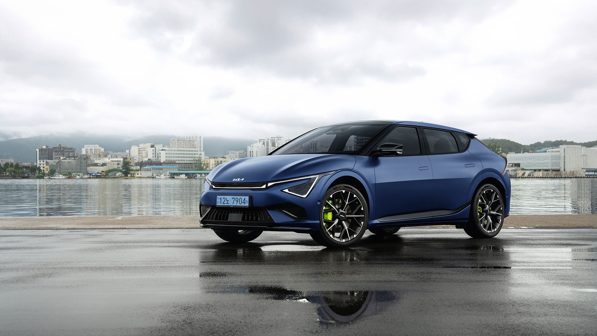 Front view of a matte blue EV6 GT parked on a waterlogged pier, with neon lime brake calipers