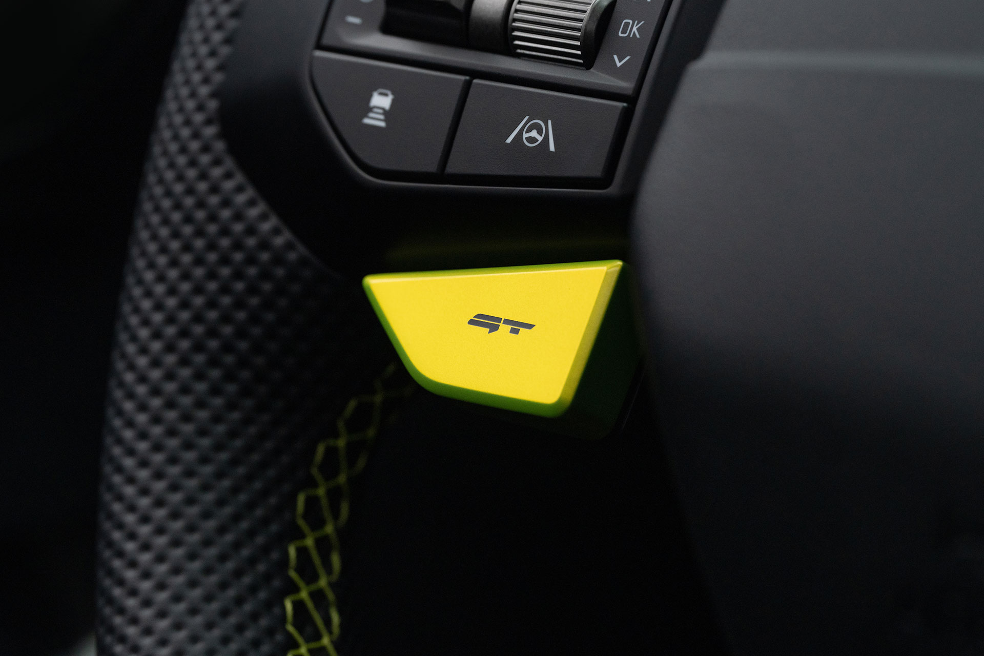 A perforated leather steering wheel with a neon-green GT drive mode button