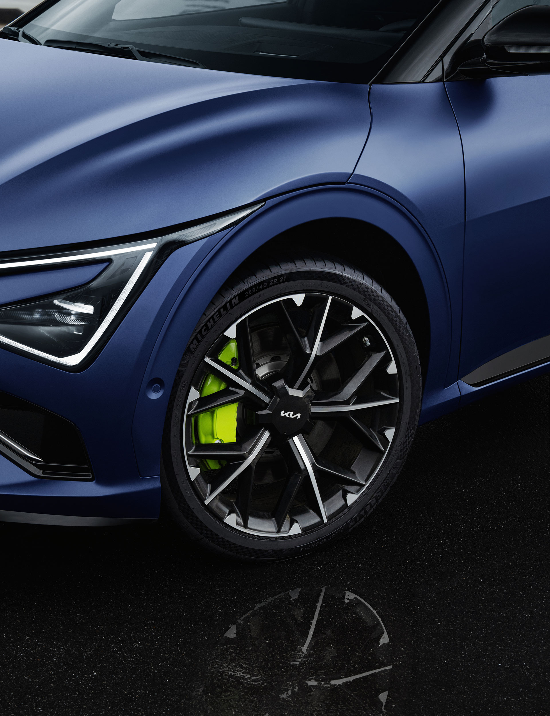 A close-up of the 21-inch wheel and neon-green brake caliper of a matte blue EV6 GT